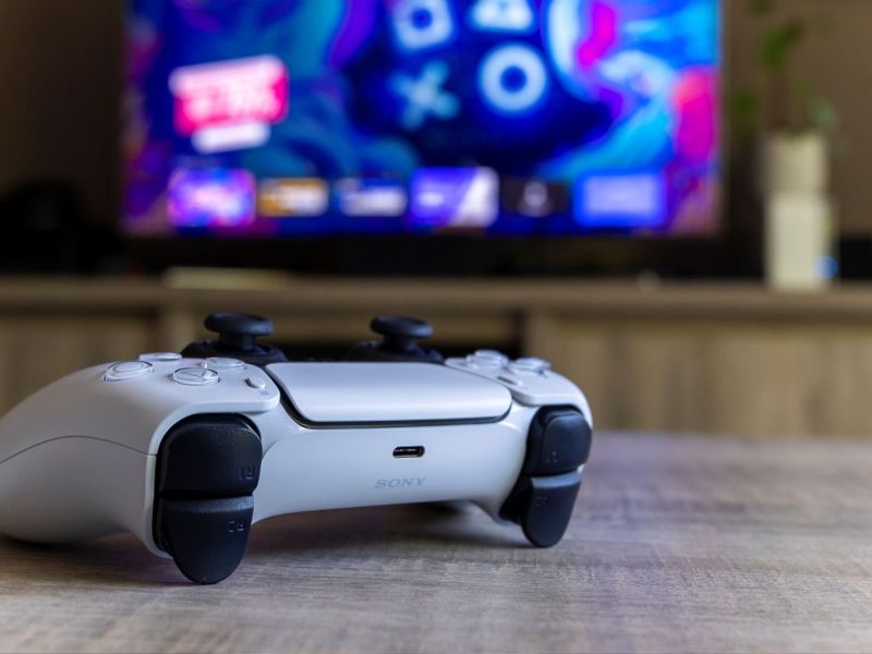 PS5-Controller vor einem Bildschirm mit PlayStation-Symbolen.